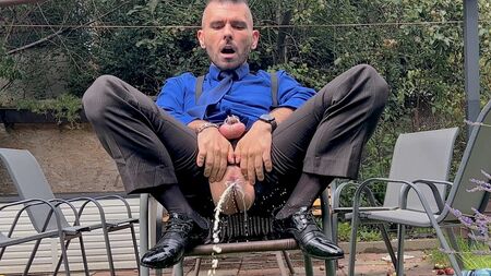 Un homme en costume, le pénis coincé dans son pantalon, se caresse le clitoris et pisse en public, vêtu de chaussettes transparentes